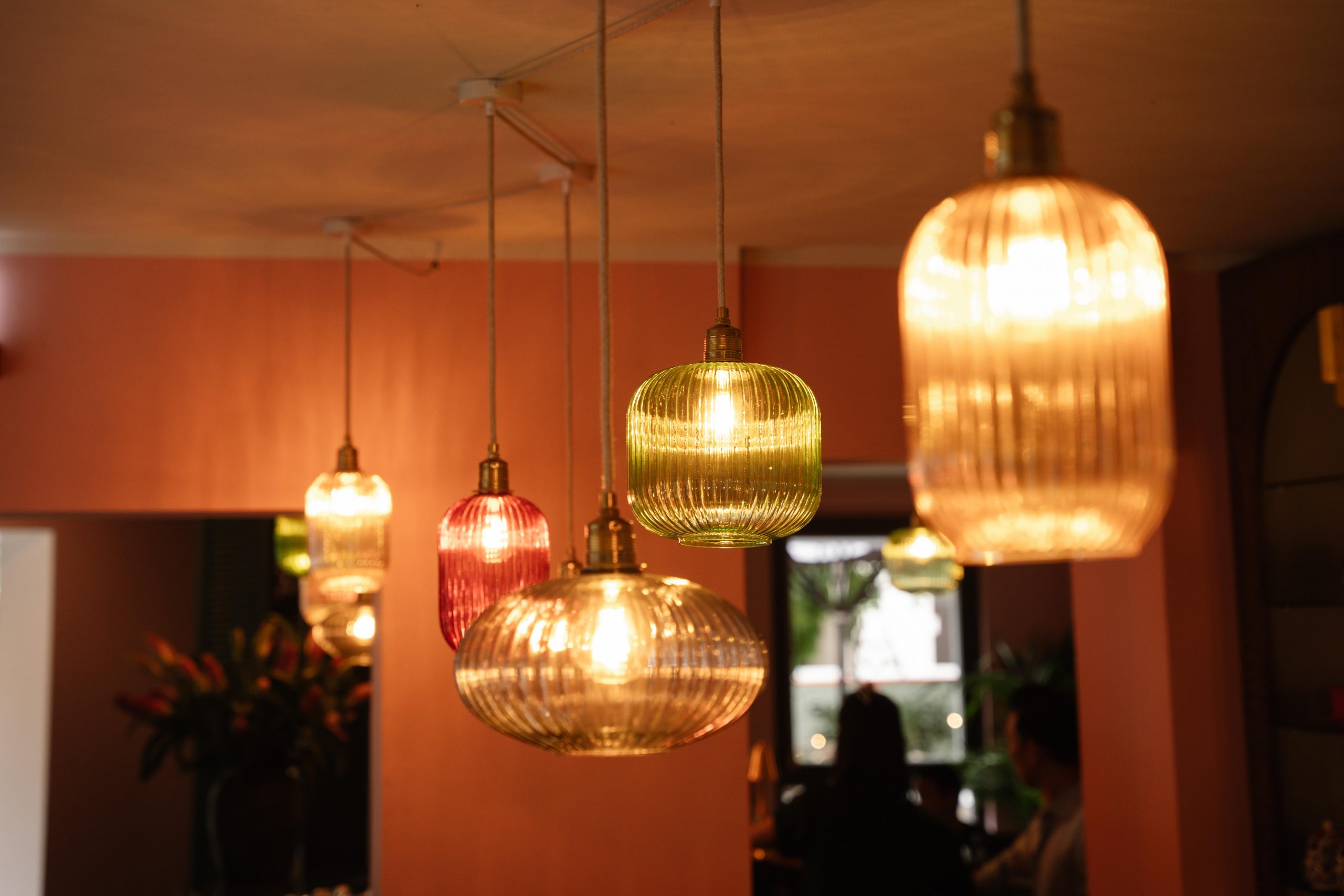 Several ribbed glass pendant lights in amber, red, and green hanging over a dining area in a cozy restaurant.