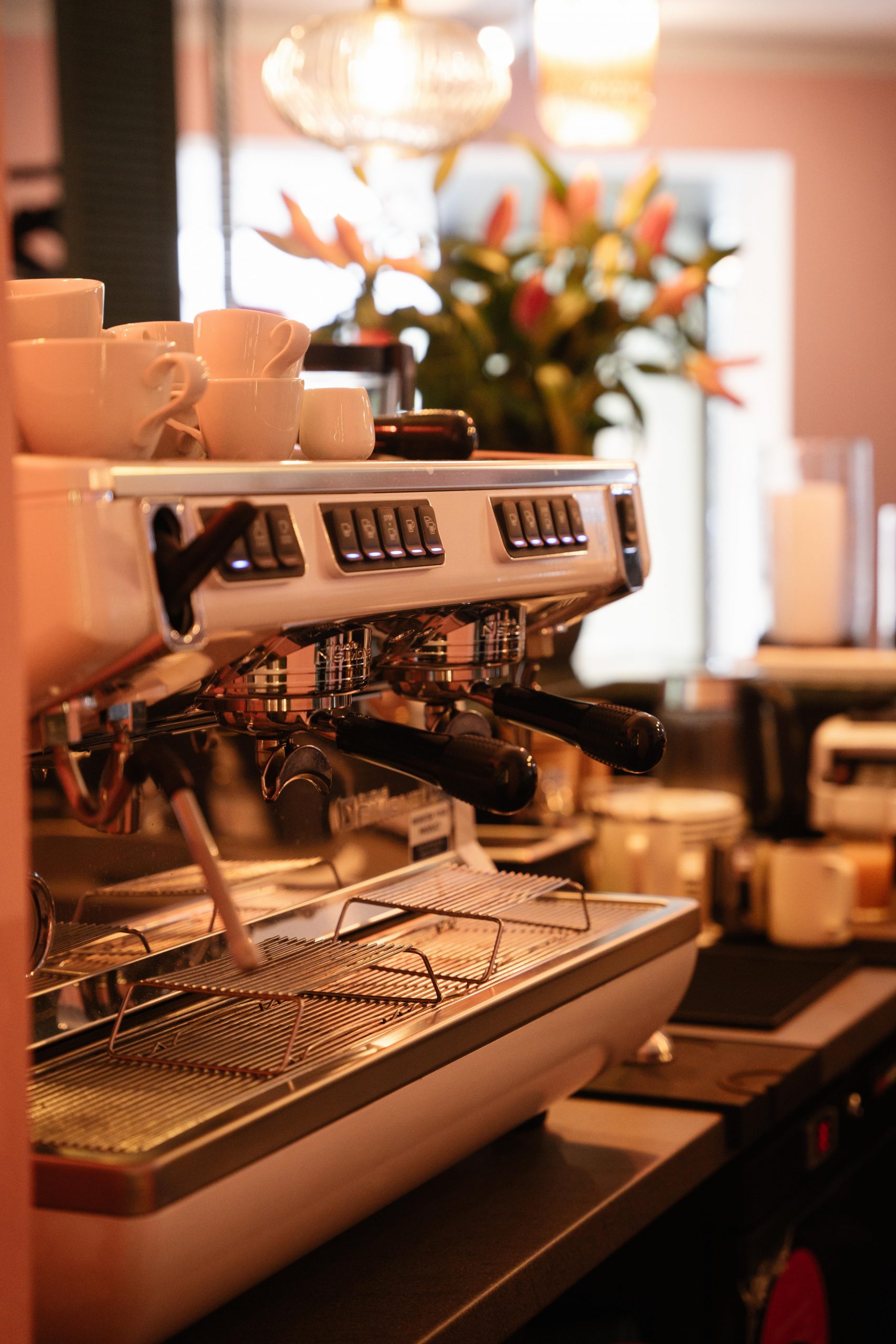 Espresso machine with several white cups stacked on top, bar area of a cafe in the background.